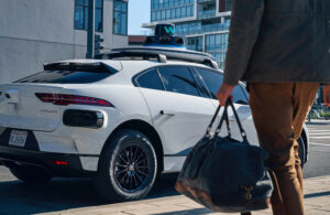A person walking towards a Waymo vehicle with a bag.